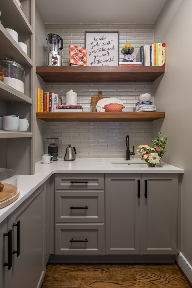 This is an example of a transitional l-shaped kitchen pantry in Raleigh with an undermount sink, recessed-panel cabinets, grey cabinets, grey splashback, glass tile splashback, brown floor, white benchtop and medium hardwood floors.