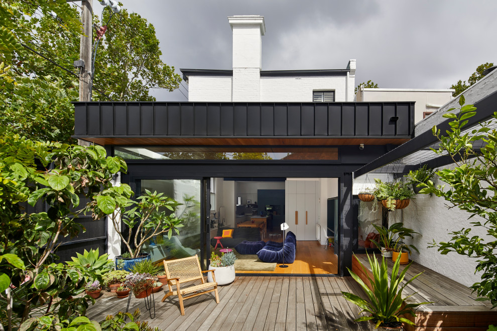 This is an example of a small backyard and ground level deck in Melbourne with a container garden, a pergola and metal railing.