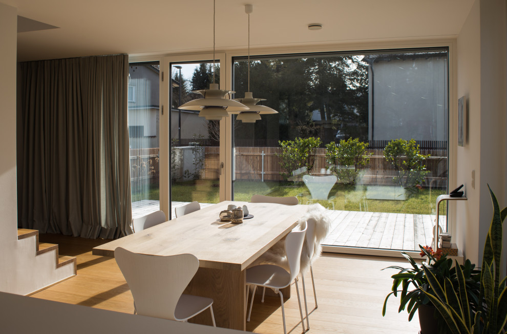 Cette image montre une salle à manger ouverte sur la cuisine design avec un mur blanc, un sol en bois brun et un sol marron.