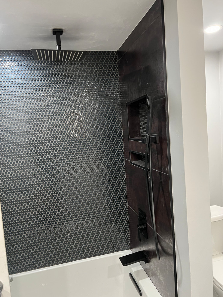 This is an example of a mid-sized modern 3/4 bathroom in Phoenix with flat-panel cabinets, white cabinets, a drop-in tub, an alcove shower, a two-piece toilet, black tile, ceramic tile, black walls, ceramic floors, an undermount sink, engineered quartz benchtops, black floor, an open shower, white benchtops, a niche, a single vanity and a built-in vanity.