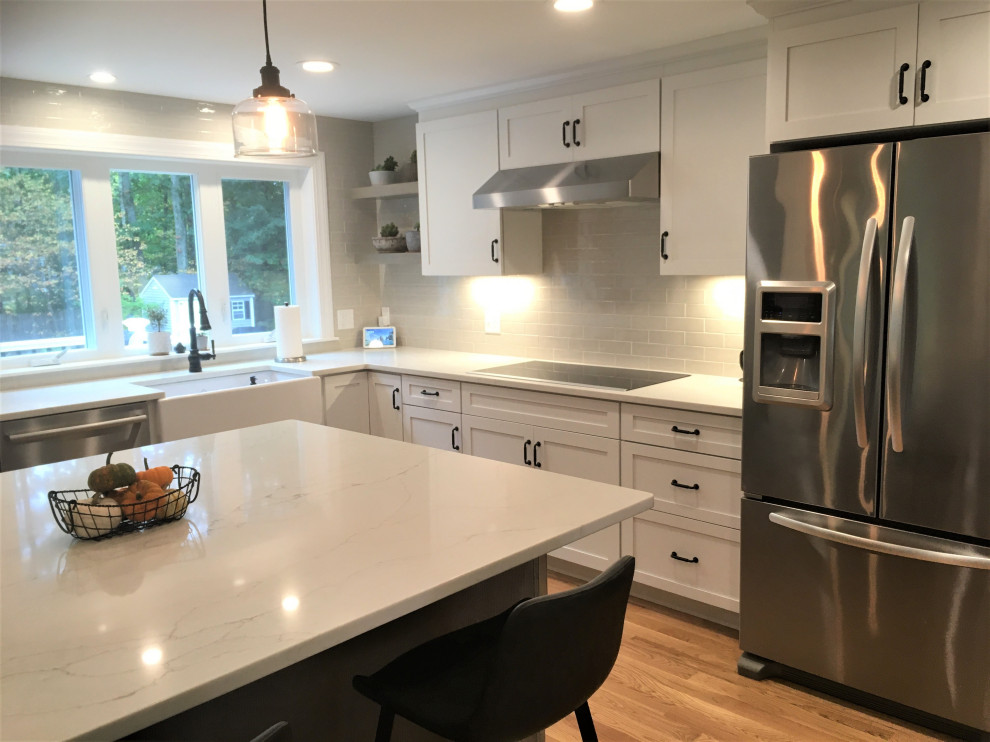 Inspiration for a large transitional u-shaped light wood floor and brown floor eat-in kitchen remodel in Boston with a farmhouse sink, shaker cabinets, white cabinets, quartz countertops, beige backsplash, subway tile backsplash, stainless steel appliances, an island and white countertops
