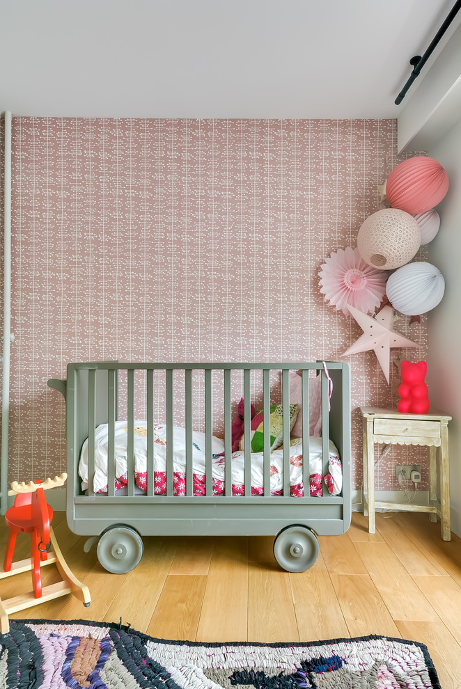 This is an example of a mid-sized eclectic nursery for girls in Paris with pink walls, light hardwood floors and beige floor.