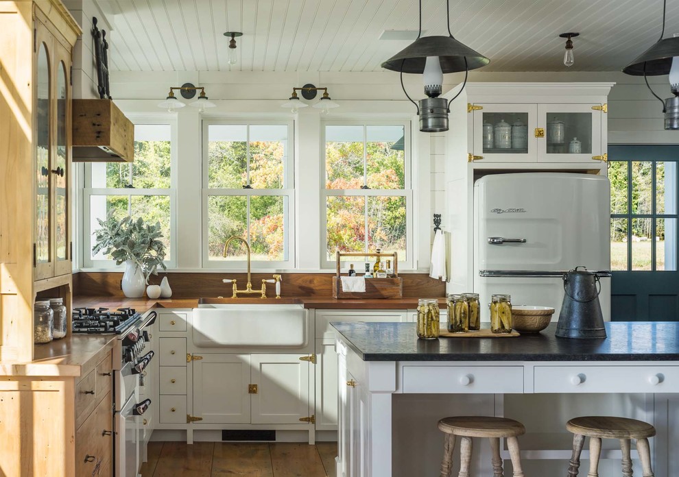 Inspiration for a country l-shaped eat-in kitchen in Burlington with a farmhouse sink, shaker cabinets, white cabinets, wood benchtops, white splashback, window splashback, white appliances, medium hardwood floors, with island, brown floor and brown benchtop.
