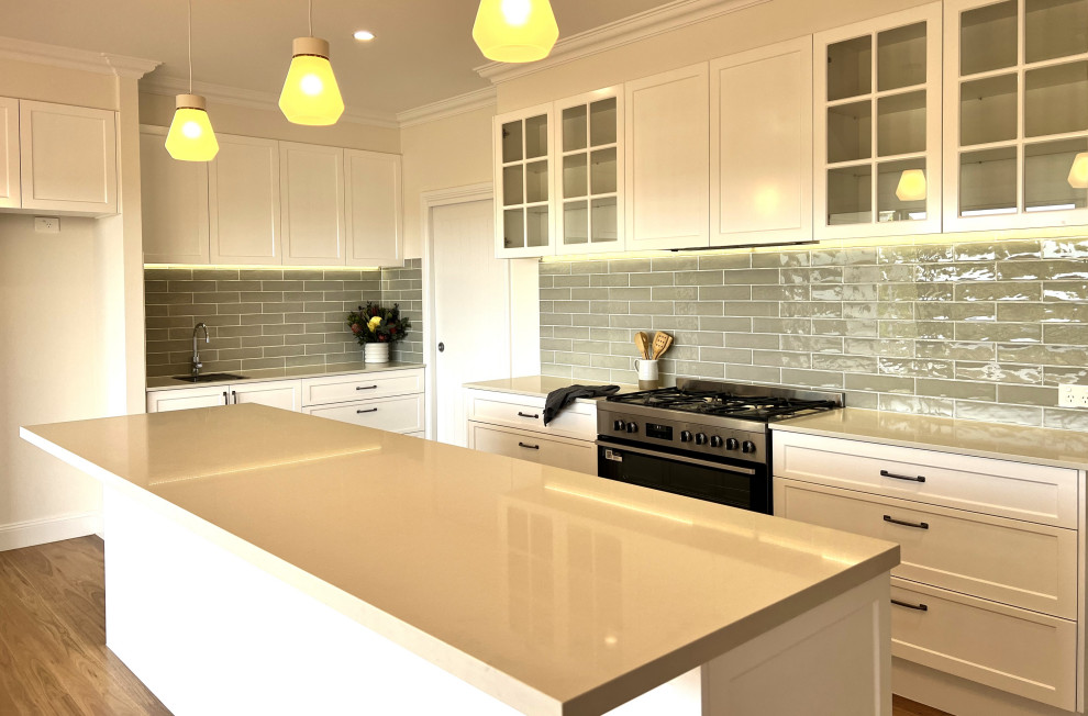 Inspiration for a country l-shaped kitchen pantry in Sunshine Coast with shaker cabinets, white cabinets, grey splashback, subway tile splashback, light hardwood floors, with island and brown floor.