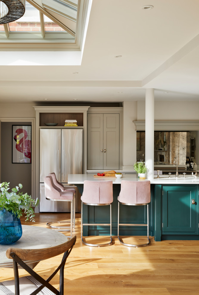 Small open plan kitchen in Essex with a drop-in sink, recessed-panel cabinets, turquoise cabinets, quartzite benchtops, metallic splashback, mirror splashback, stainless steel appliances, medium hardwood floors, a peninsula, brown floor, white benchtop and recessed.