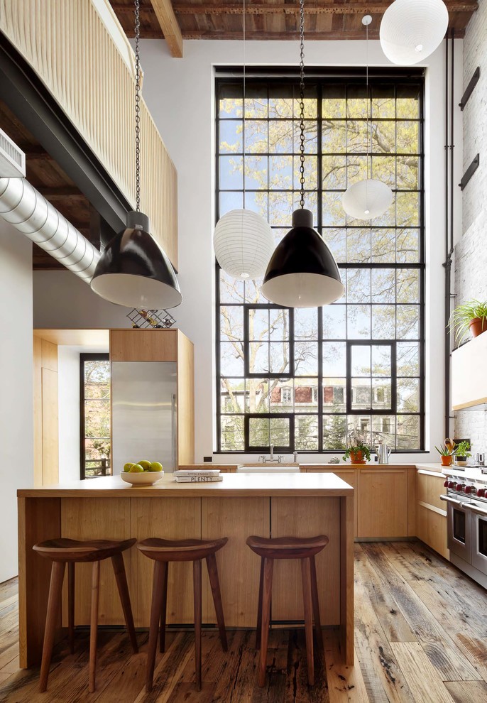 Large industrial eat-in kitchen in New York with flat-panel cabinets, brown cabinets, white splashback, medium hardwood floors and with island.