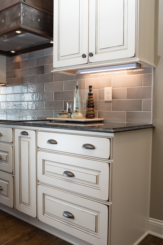Large mountain style l-shaped dark wood floor and brown floor eat-in kitchen photo with a farmhouse sink, raised-panel cabinets, granite countertops, gray backsplash, ceramic backsplash, black appliances, an island and white cabinets