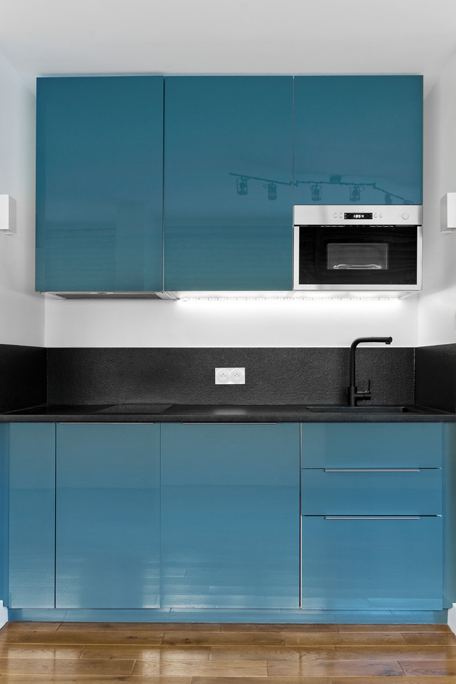 Photo of a small scandinavian single-wall eat-in kitchen in Paris with an undermount sink, beaded inset cabinets, blue cabinets, granite benchtops, black splashback, panelled appliances, medium hardwood floors, no island and black benchtop.