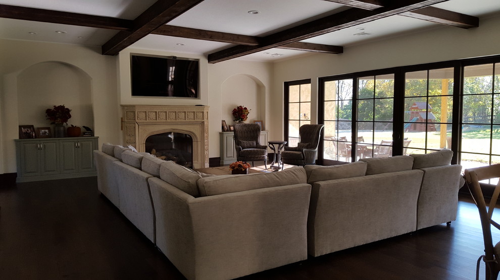 This is an example of a mid-sized mediterranean open concept living room in New York with beige walls, dark hardwood floors, a standard fireplace, a concrete fireplace surround, a wall-mounted tv and brown floor.