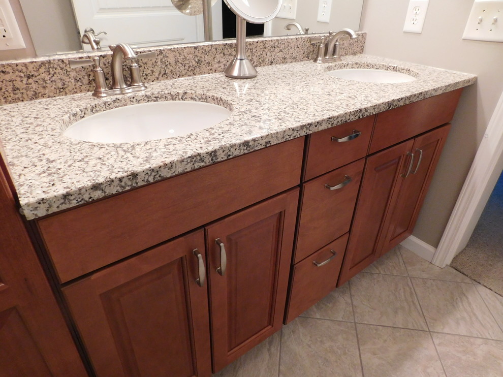 Corner bathtub - large transitional master gray tile and ceramic tile ceramic tile corner bathtub idea with raised-panel cabinets, medium tone wood cabinets, a two-piece toilet, beige walls, an undermount sink and granite countertops