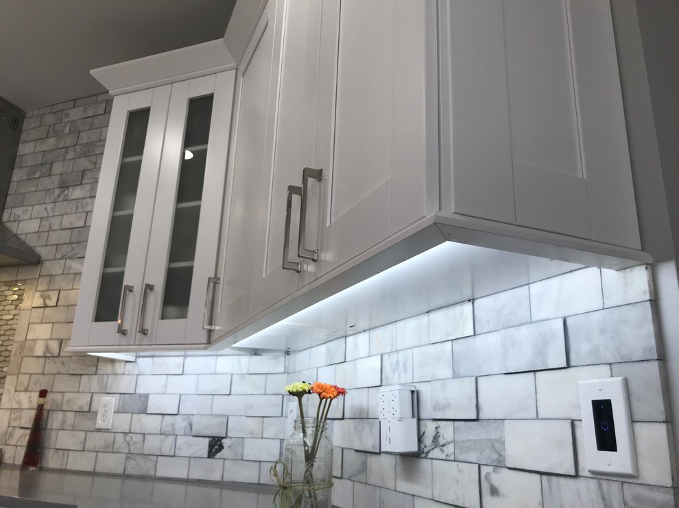 Inspiration for a large transitional single-wall light wood floor and gray floor eat-in kitchen remodel in Atlanta with a farmhouse sink, shaker cabinets, white cabinets, quartzite countertops, white backsplash, marble backsplash, stainless steel appliances, an island and white countertops