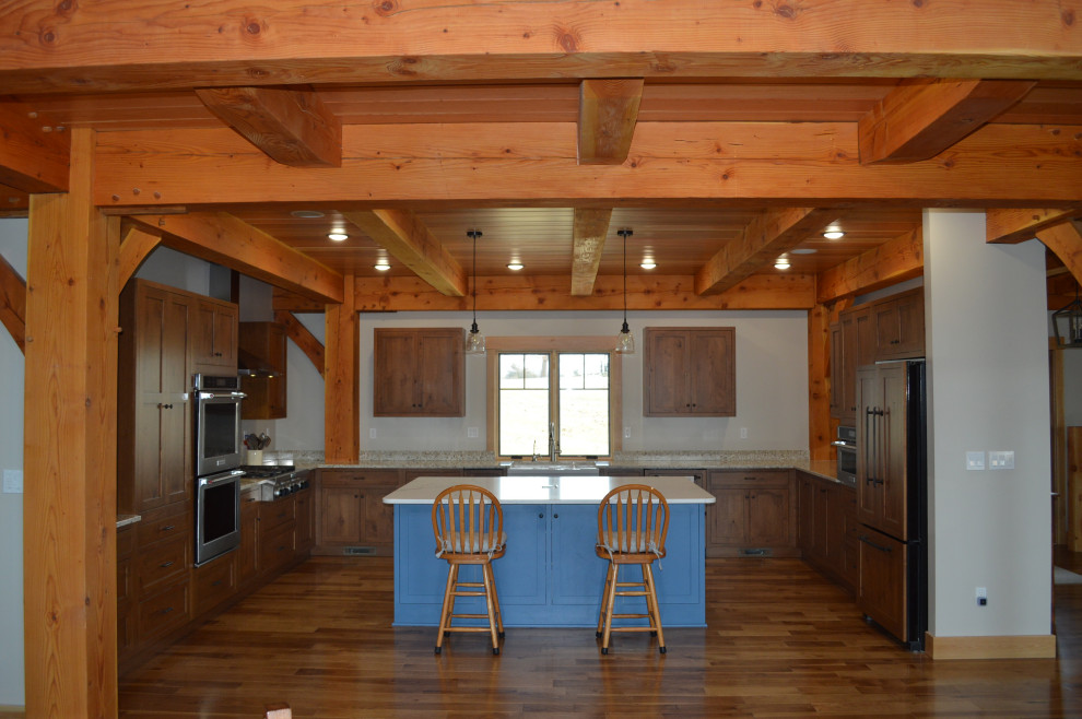 Example of a mid-sized mountain style u-shaped medium tone wood floor, brown floor and exposed beam eat-in kitchen design with a farmhouse sink, shaker cabinets, medium tone wood cabinets, paneled appliances and an island