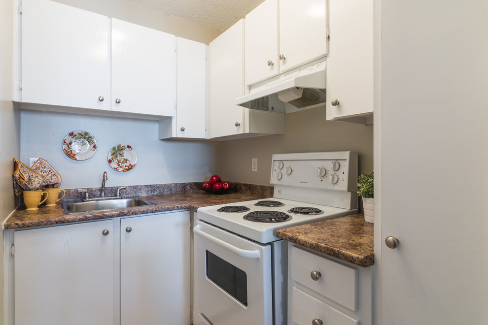 Small contemporary l-shaped separate kitchen in Montreal with a single-bowl sink, flat-panel cabinets, white cabinets, laminate benchtops, white appliances and linoleum floors.