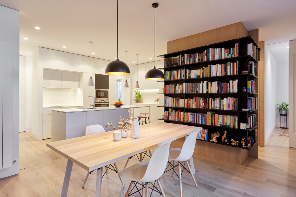 Modelo de biblioteca en casa abierta moderna grande con paredes blancas, suelo de madera en tonos medios, televisor colgado en la pared y suelo marrón