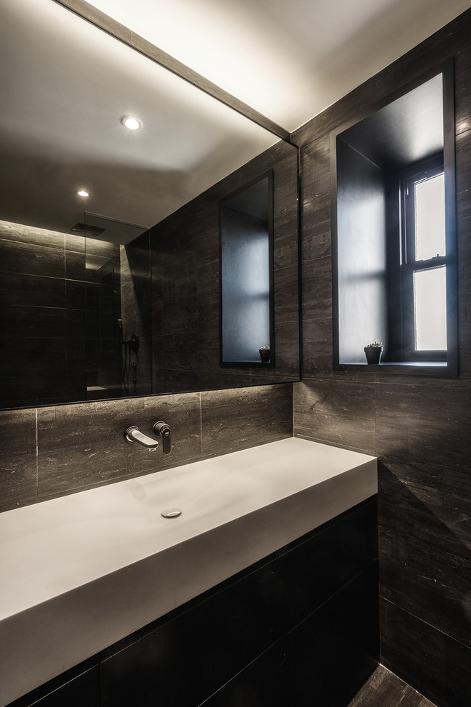 Photo of a small modern master bathroom in New York with flat-panel cabinets, black cabinets, a drop-in tub, a shower/bathtub combo, a two-piece toilet, black tile, stone slab, black walls, limestone floors, an integrated sink and solid surface benchtops.