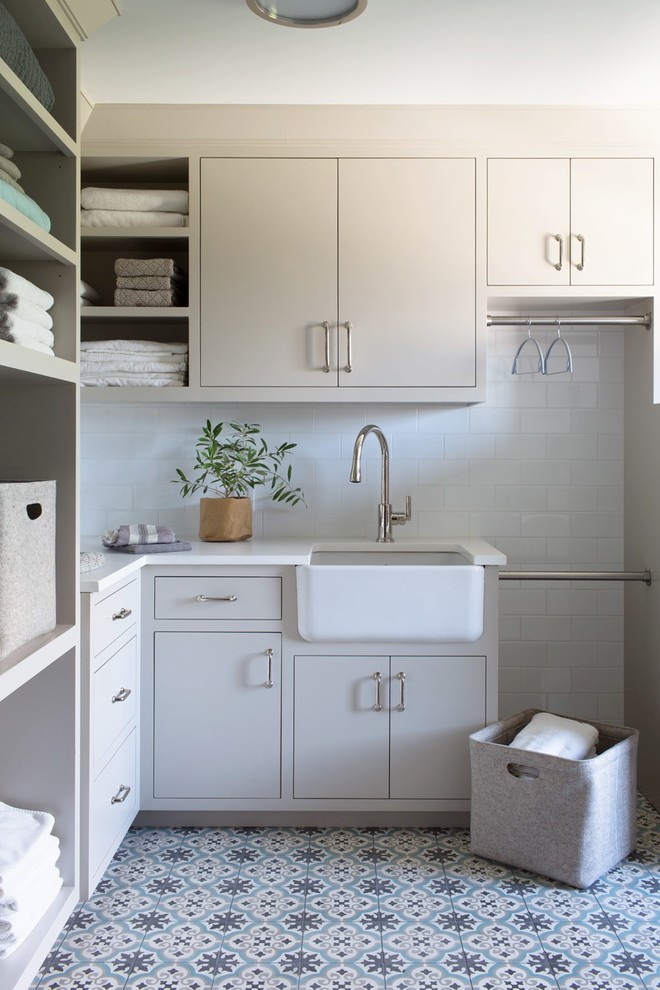 Design ideas for a mid-sized transitional l-shaped utility room in Other with a farmhouse sink, flat-panel cabinets, beige cabinets, quartzite benchtops, white walls, ceramic floors, multi-coloured floor and white benchtop.