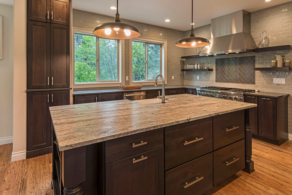 Inspiration for a large transitional l-shaped medium tone wood floor and brown floor open concept kitchen remodel with a farmhouse sink, shaker cabinets, dark wood cabinets, granite countertops, gray backsplash, subway tile backsplash, paneled appliances and an island