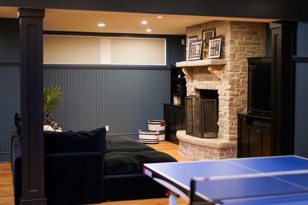 Cette photo montre un grand sous-sol chic enterré avec un bar de salon, un mur bleu, parquet clair, une cheminée standard et un manteau de cheminée en pierre.