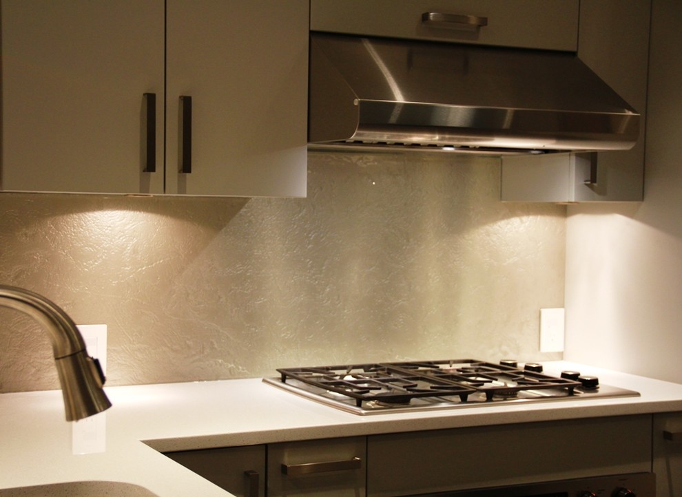 Modern inredning av ett kök och matrum, med vitt stänkskydd, glaspanel som stänkskydd och rostfria vitvaror