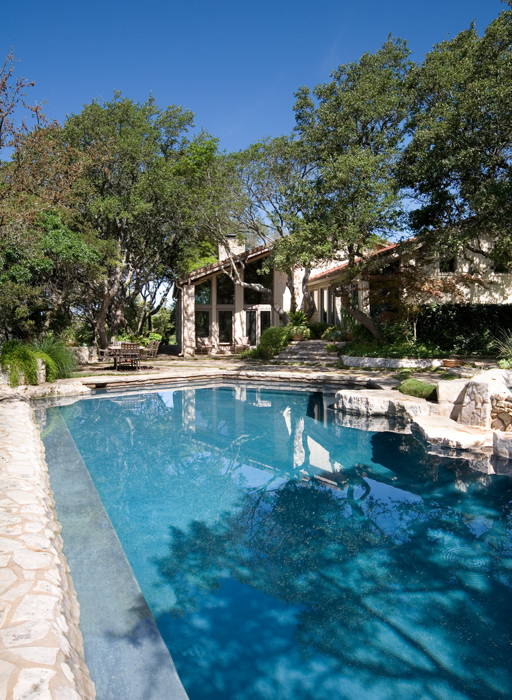 Photo of a mid-sized country backyard custom-shaped natural pool in Austin with natural stone pavers and a hot tub.