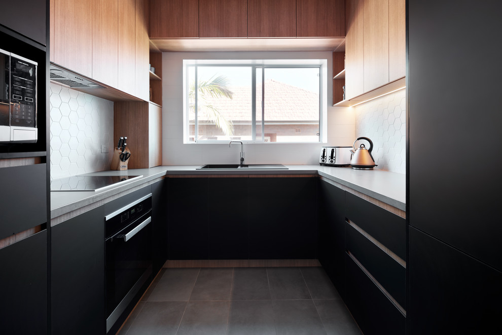 Inspiration for a contemporary u-shaped separate kitchen in Sydney with a drop-in sink, flat-panel cabinets, black cabinets, white splashback, black appliances, no island, grey floor and grey benchtop.