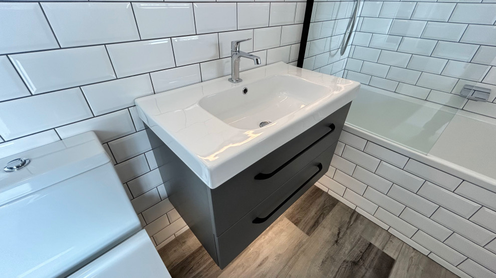 Small modern grey and white family bathroom in Hampshire with flat-panel cabinets, grey cabinets, a built-in bath, a shower/bath combination, a two-piece toilet, white tiles, porcelain tiles, white walls, vinyl flooring, an integrated sink, grey floors, a hinged door, a laundry area, a single sink and a floating vanity unit.