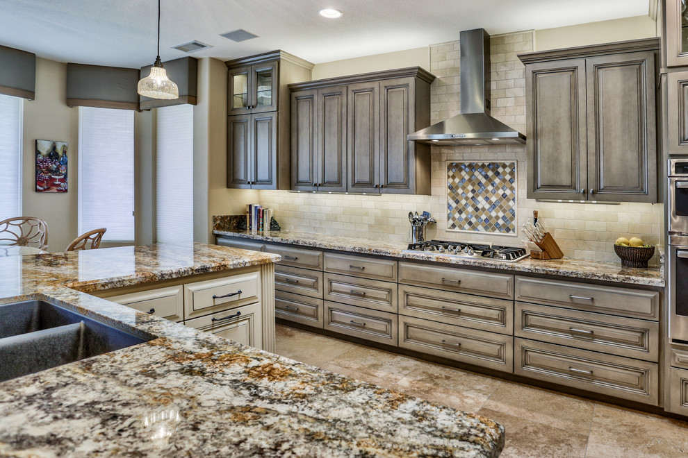 Large transitional l-shaped open plan kitchen in Phoenix with an undermount sink, raised-panel cabinets, distressed cabinets, granite benchtops, beige splashback, stone tile splashback, stainless steel appliances, travertine floors, with island, beige floor and multi-coloured benchtop.
