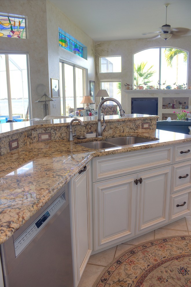 Photo of a mid-sized beach style l-shaped kitchen in Miami with an undermount sink, raised-panel cabinets, white cabinets, granite benchtops, multi-coloured splashback, stainless steel appliances, ceramic floors, with island, beige floor and multi-coloured benchtop.