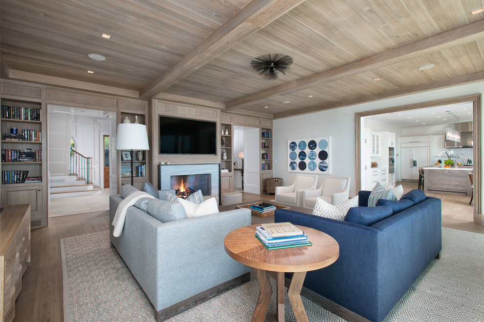 Large beach style enclosed family room in New York with a library, white walls, light hardwood floors, a standard fireplace, a wall-mounted tv and a stone fireplace surround.
