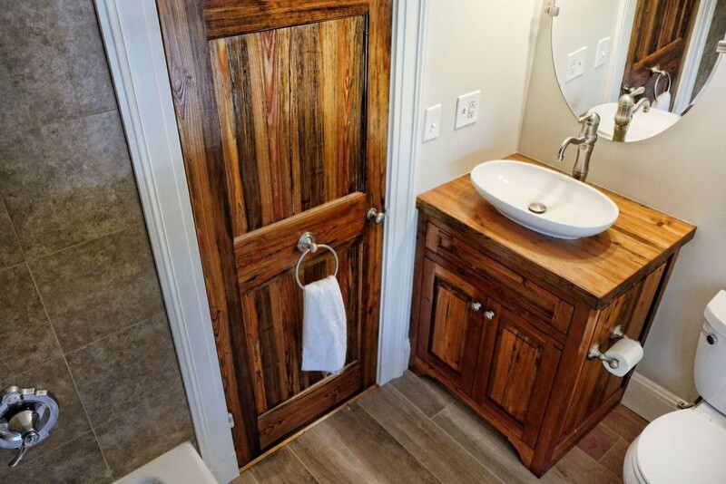 This is an example of a mid-sized country 3/4 bathroom in Bridgeport with raised-panel cabinets, brown cabinets, a drop-in tub, a shower/bathtub combo, a two-piece toilet, beige tile, ceramic tile, white walls, vinyl floors, a vessel sink, wood benchtops, brown floor, a shower curtain and blue benchtops.