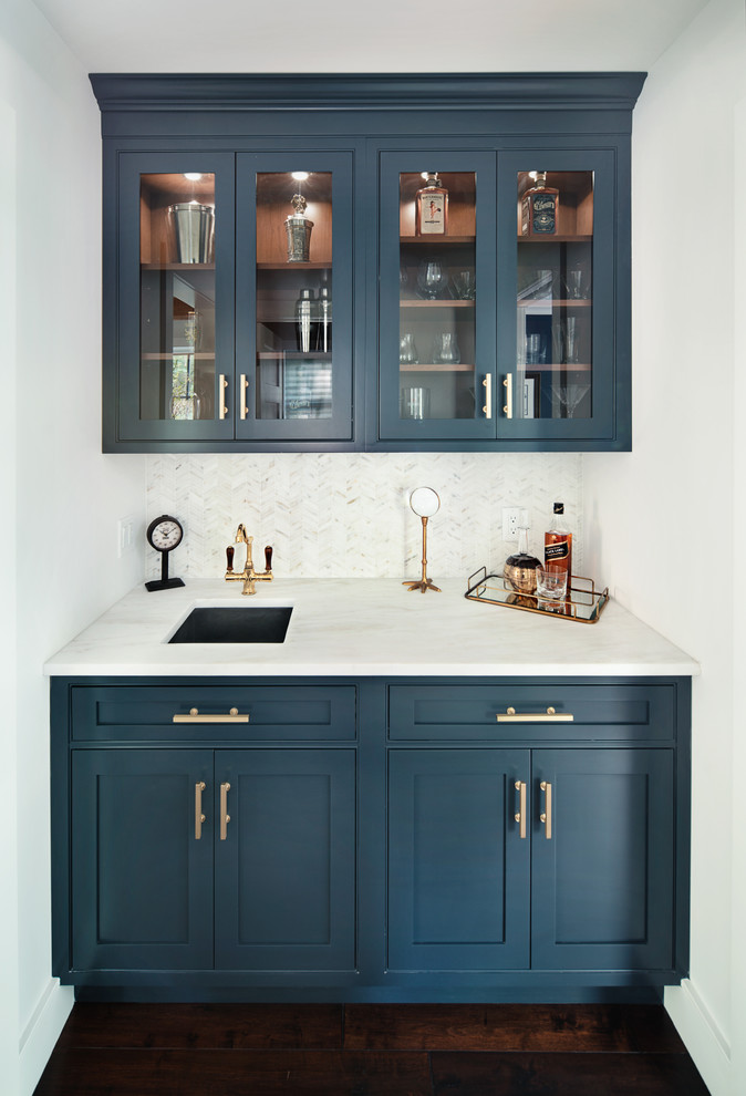 Small transitional single-wall wet bar in New York with glass-front cabinets, blue cabinets, marble benchtops, white splashback, ceramic splashback and dark hardwood floors.