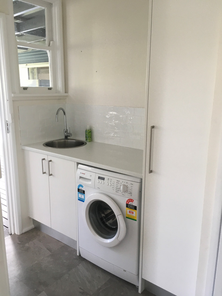 Small contemporary single-wall dedicated laundry room in Sydney with a single-bowl sink, flat-panel cabinets, white cabinets, laminate benchtops, white splashback, ceramic splashback and grey benchtop.