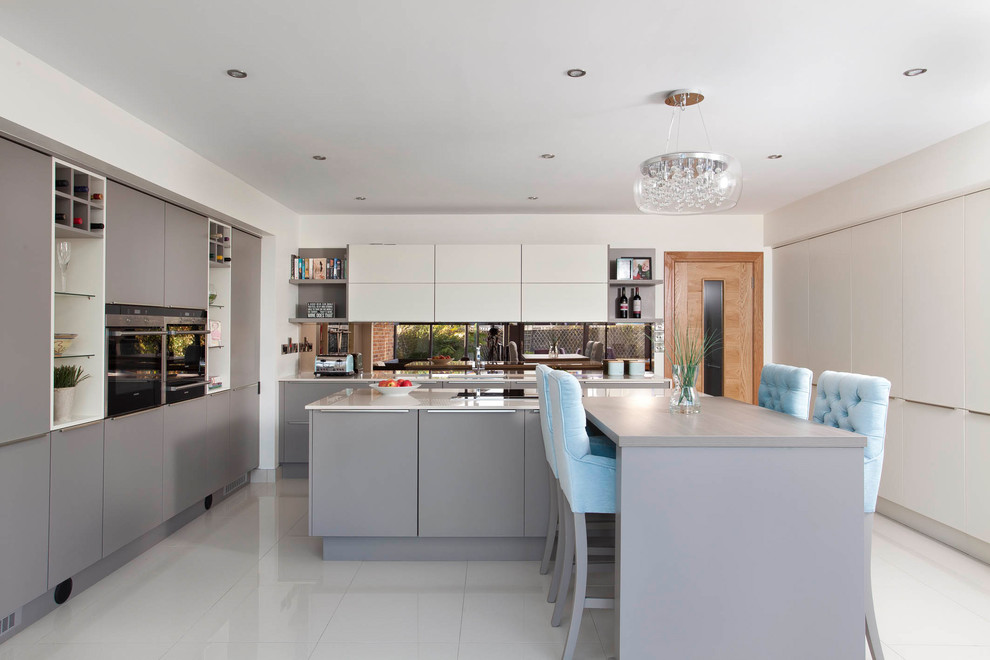 Design ideas for a mid-sized contemporary galley eat-in kitchen in Dublin with flat-panel cabinets, grey cabinets, quartzite benchtops, black appliances, with island, metallic splashback, mirror splashback and white floor.