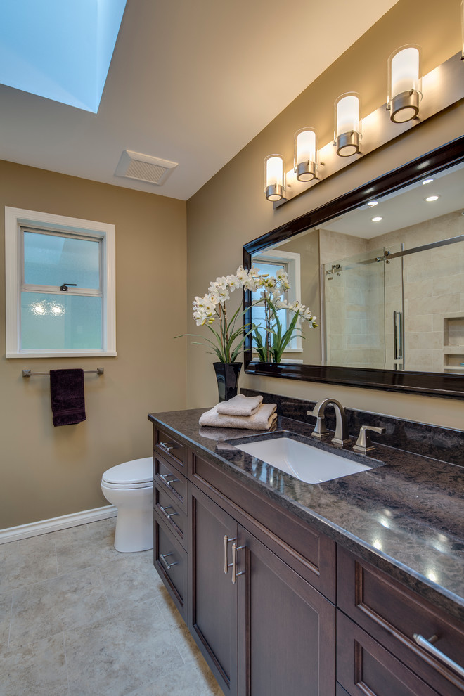 This is an example of a mid-sized contemporary kids bathroom in Vancouver with recessed-panel cabinets, dark wood cabinets, an alcove shower, a one-piece toilet, beige tile, stone tile, brown walls, linoleum floors, an undermount sink and granite benchtops.
