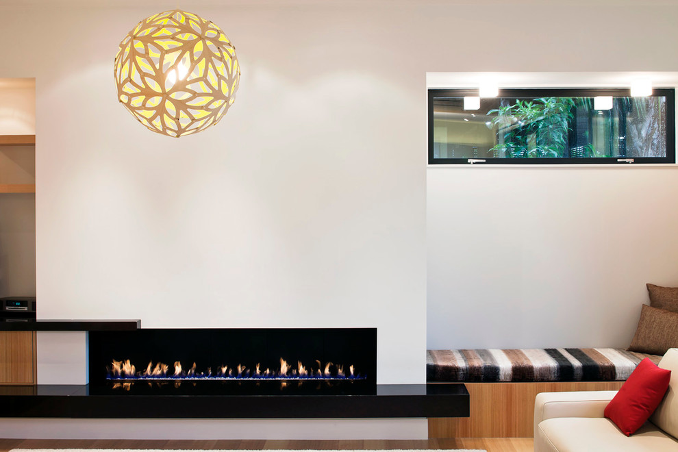 This is an example of a contemporary living room in Auckland with white walls, a ribbon fireplace and no tv.