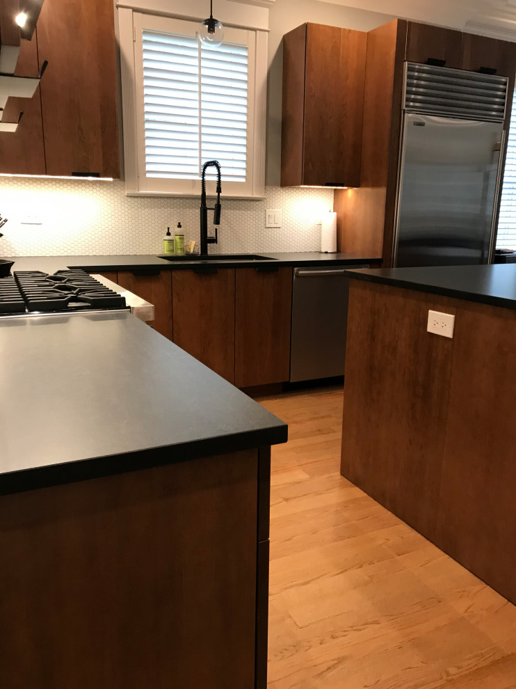 Photo of a large midcentury l-shaped kitchen/diner in Chicago with a submerged sink, flat-panel cabinets, brown cabinets, engineered stone countertops, white splashback, ceramic splashback, stainless steel appliances, medium hardwood flooring, an island, brown floors and black worktops.