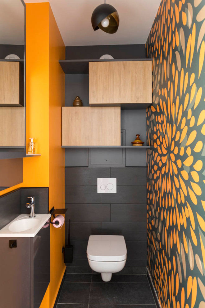Design ideas for a medium sized contemporary cloakroom in Paris with flat-panel cabinets, light wood cabinets, a wall mounted toilet, black tiles, ceramic tiles, orange walls, ceramic flooring, a wall-mounted sink, solid surface worktops, grey floors, white worktops and a floating vanity unit.