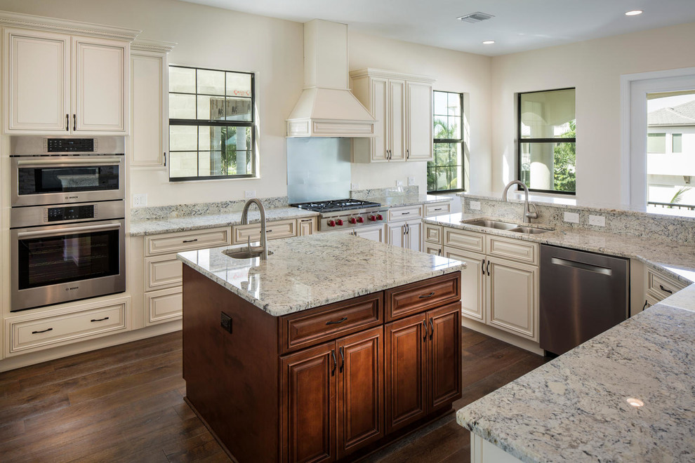 Inspiration for a large mediterranean l-shaped open plan kitchen in Tampa with an undermount sink, raised-panel cabinets, white cabinets, granite benchtops, white splashback, stainless steel appliances, medium hardwood floors and with island.