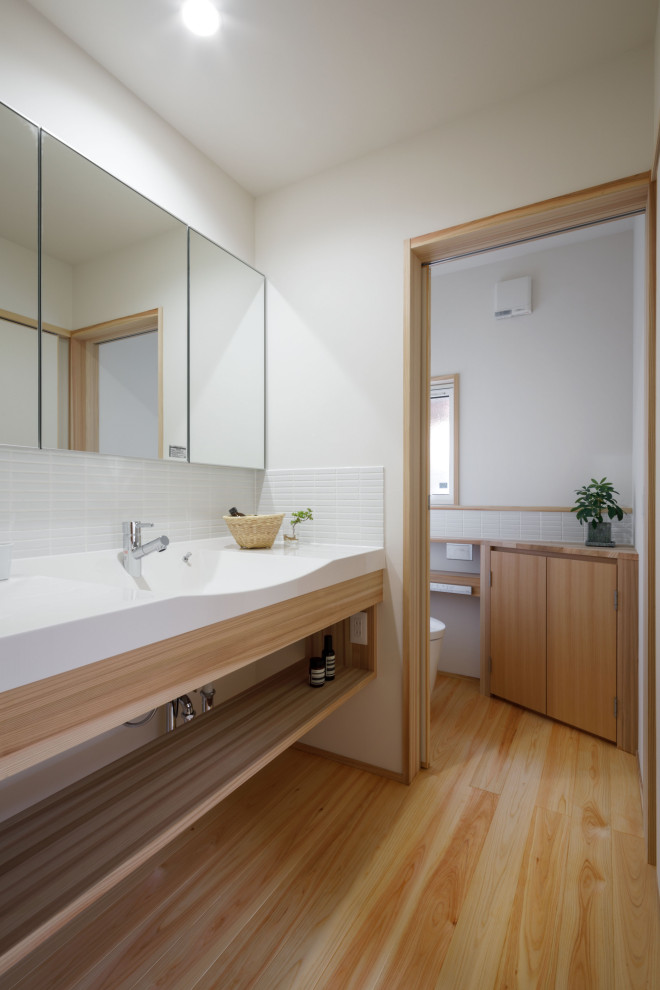 На фото: туалет в скандинавском стиле с открытыми фасадами, белыми фасадами, белой плиткой, белыми стенами, монолитной раковиной, коричневым полом, белой столешницей и встроенной тумбой с