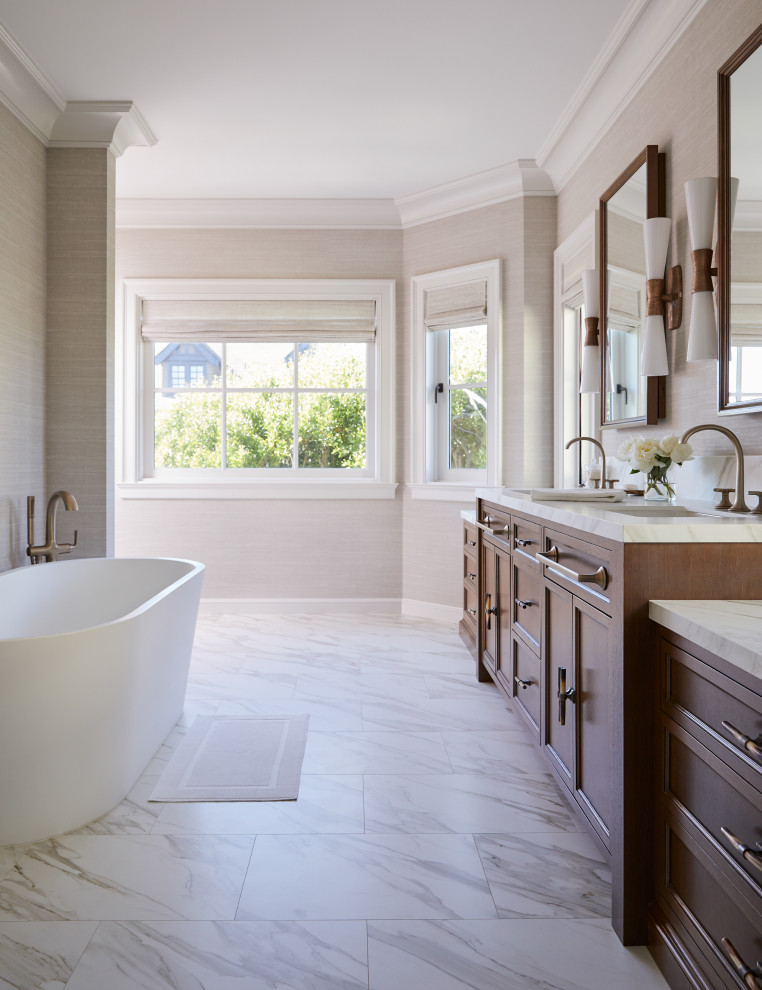 Photo of a large transitional master bathroom in San Francisco with recessed-panel cabinets, brown cabinets, a freestanding tub, a double shower, a one-piece toilet, white tile, marble, beige walls, marble floors, an undermount sink, marble benchtops, white floor, a hinged shower door, white benchtops, a double vanity, a built-in vanity and wallpaper.