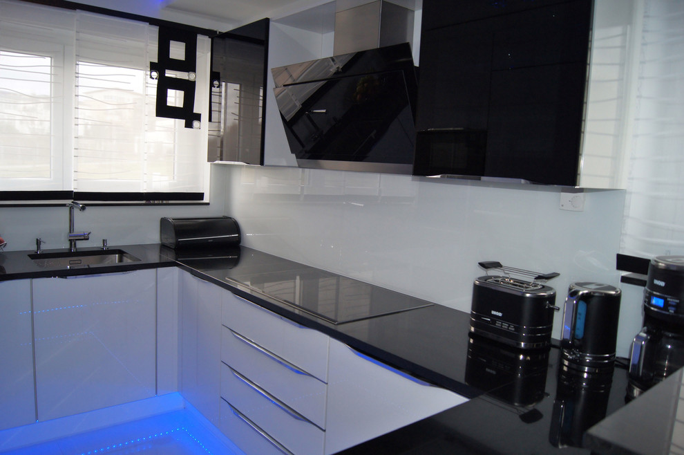 This is an example of a small contemporary u-shaped open plan kitchen in Stuttgart with flat-panel cabinets, black cabinets, solid surface benchtops, white splashback, glass sheet splashback, no island, a single-bowl sink, black appliances, ceramic floors and white floor.