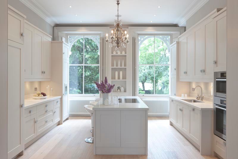 Photo of a large traditional galley open plan kitchen in London with recessed-panel cabinets, white cabinets, quartzite benchtops, white splashback, ceramic splashback, stainless steel appliances, dark hardwood floors, multiple islands and white benchtop.