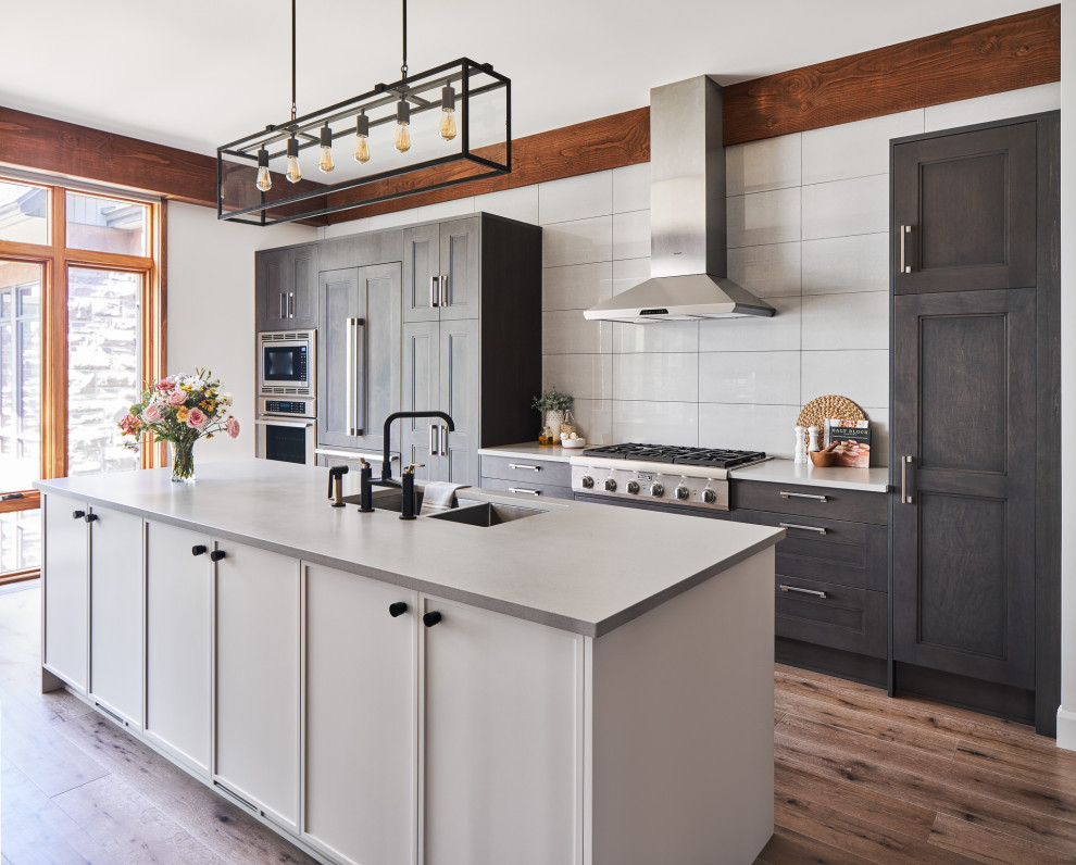 Country galley kitchen in Ottawa with an undermount sink, recessed-panel cabinets, dark wood cabinets, white splashback, panelled appliances, medium hardwood floors, with island, brown floor and white benchtop.