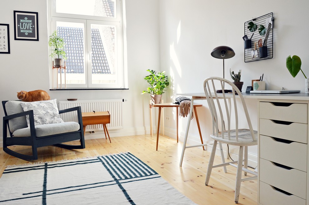 Inspiration for a mid-sized scandinavian study room in Dusseldorf with white walls, light hardwood floors, a freestanding desk, no fireplace and brown floor.