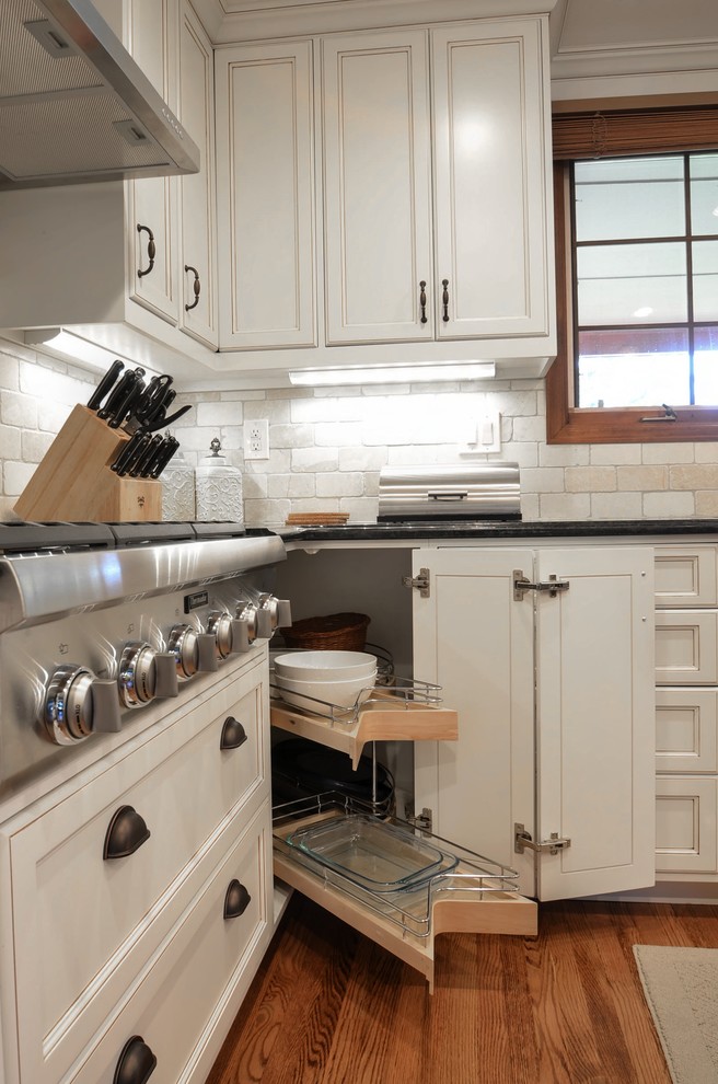 Eat-in kitchen - mid-sized transitional u-shaped medium tone wood floor eat-in kitchen idea in Denver with an undermount sink, recessed-panel cabinets, white cabinets, granite countertops, beige backsplash, stone tile backsplash, stainless steel appliances and an island