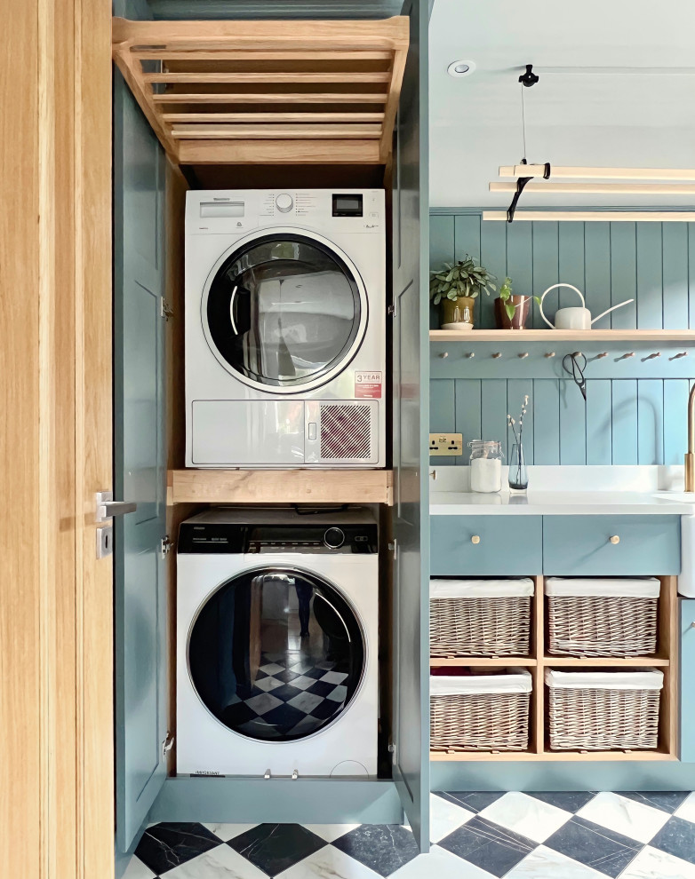 Design ideas for a small country utility room in Other with a belfast sink, shaker cabinets, blue cabinets, quartz worktops, blue walls, porcelain flooring, a stacked washer and dryer and white worktops.