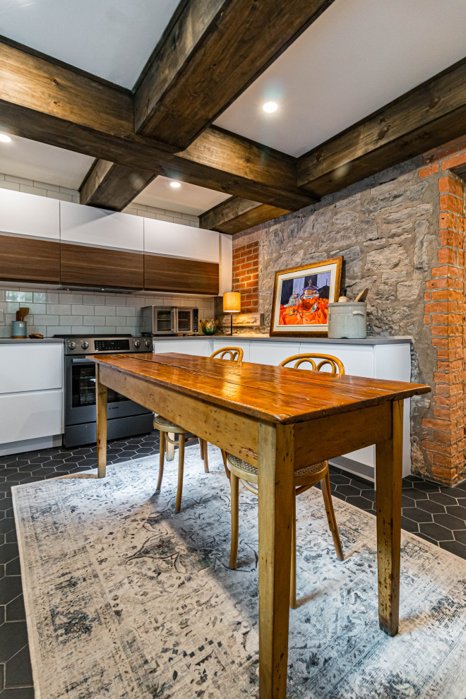 Inspiration for a mid-sized rustic u-shaped ceramic tile, black floor and exposed beam eat-in kitchen remodel in Toronto with a farmhouse sink, flat-panel cabinets, white cabinets, quartz countertops, white backsplash, subway tile backsplash, stainless steel appliances, an island and gray countertops