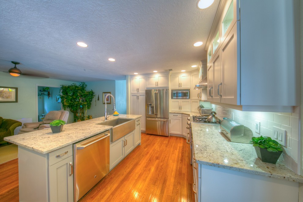 Inspiration for a mid-sized transitional light wood floor enclosed kitchen remodel in Orlando with a farmhouse sink, shaker cabinets, gray cabinets, granite countertops, white backsplash, subway tile backsplash, stainless steel appliances and an island