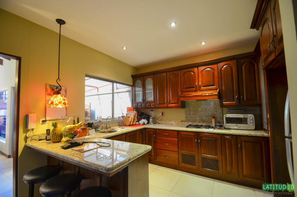 Inspiration for a small rustic u-shaped porcelain tile home design remodel with a drop-in sink, flat-panel cabinets, light wood cabinets, granite countertops, beige backsplash, ceramic backsplash, white appliances and an island
