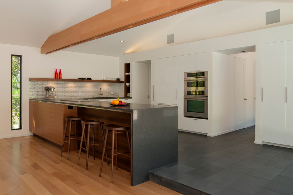 Photo of a contemporary l-shaped kitchen in San Francisco with flat-panel cabinets, white cabinets, panelled appliances, white splashback and subway tile splashback.